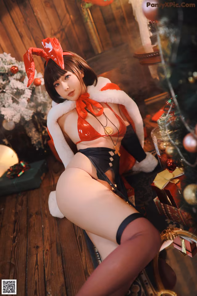 A woman in a red and black outfit sitting next to a Christmas tree.