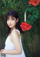 A woman in a white dress standing in front of red flowers.