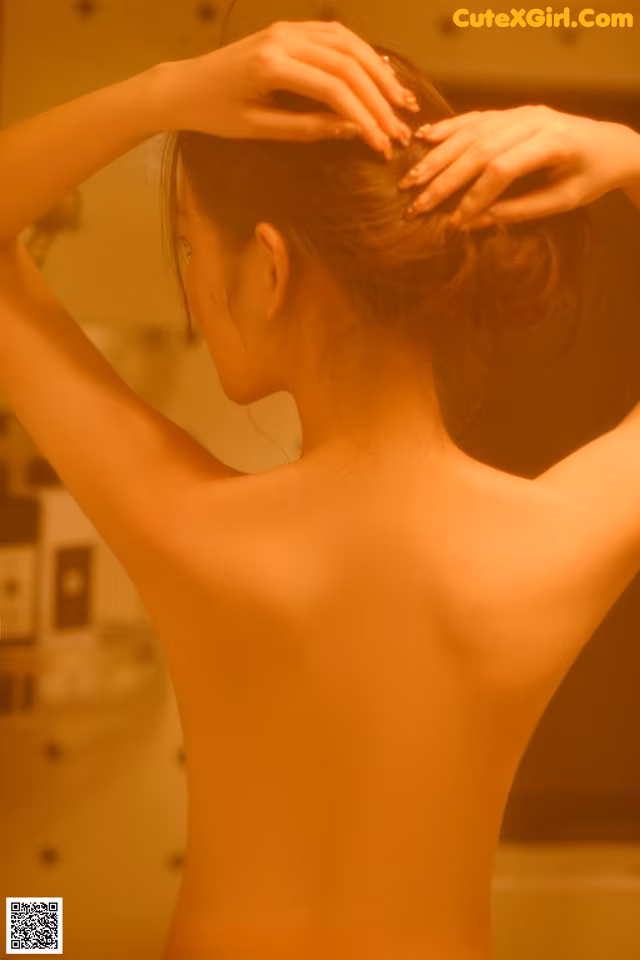 A naked woman standing in front of a mirror with her hands on her head.