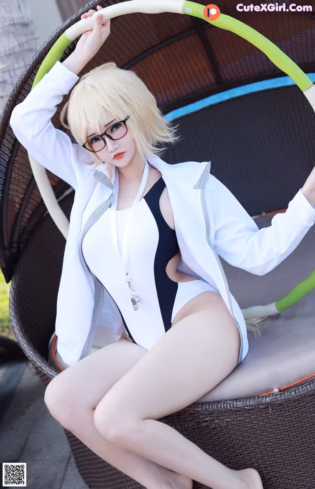 A woman in a white jacket and black and white bathing suit sitting on a wicker chair.