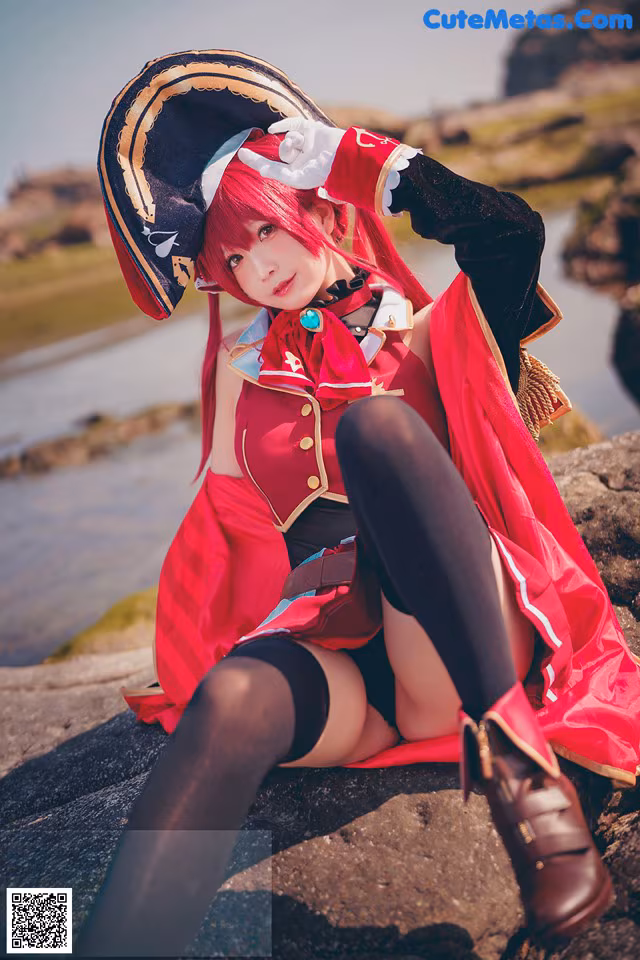 A woman in a pirate costume sitting on a rock by the water.