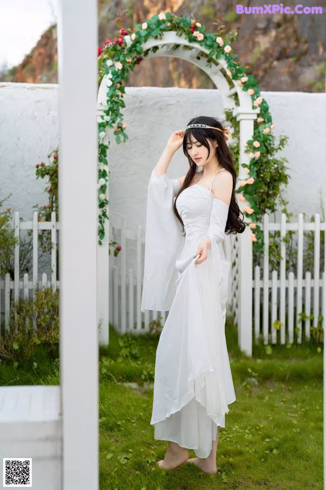 A woman in a white dress standing in front of a white fence.