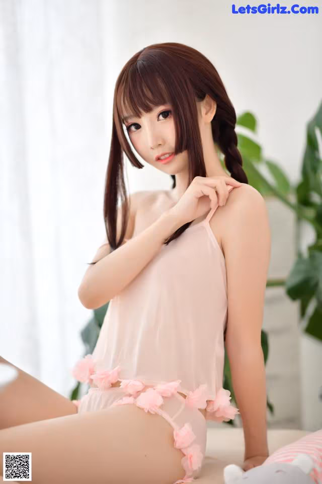 A woman in a pink lingerie sitting on a bed.