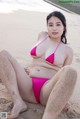 A woman in a pink bikini sitting on a beach.