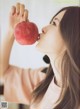 A woman holding an apple in front of her face.