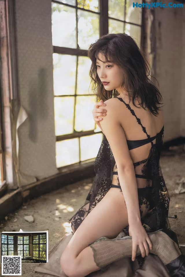 A woman in a black lingerie sitting on a window sill.