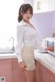 A woman in a white shirt and skirt standing in a kitchen.