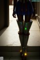 A woman in a blue skirt and boots standing on a sidewalk.