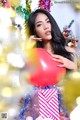 A woman holding a red heart shaped balloon in front of a Christmas tree.