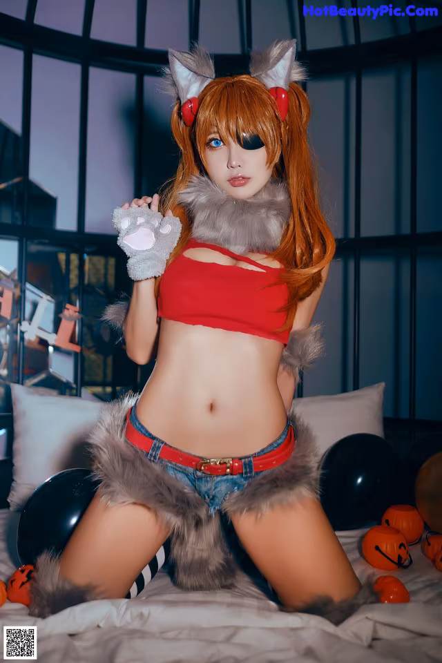 A woman in a red top and blue shorts posing on a bed.